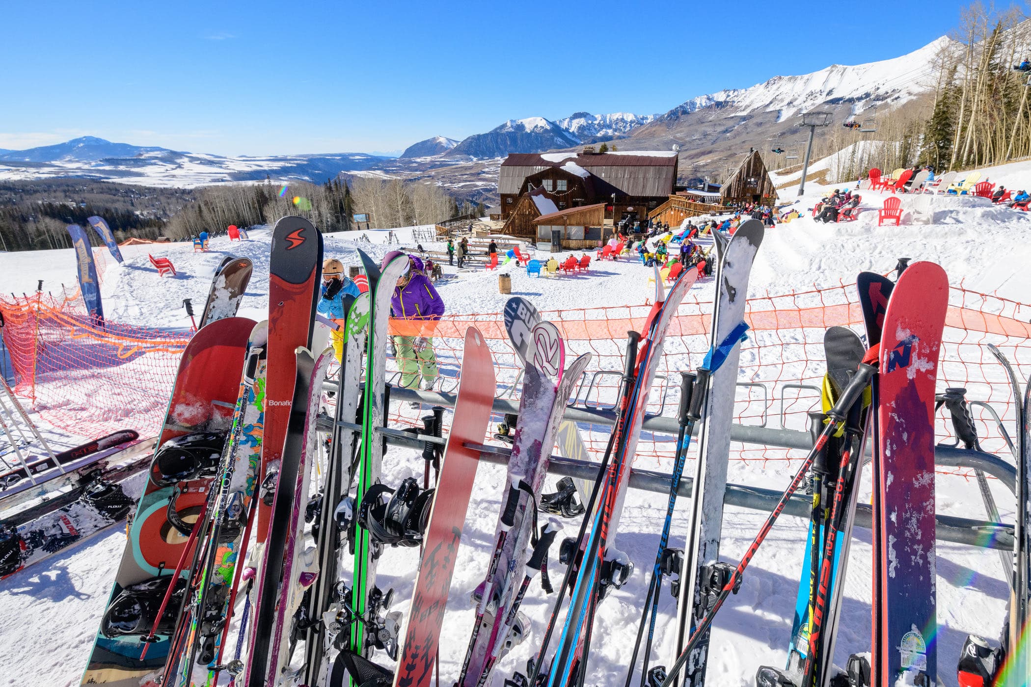 Skis and snowboards racked outside Gorrono Ranch, red chairs out on the snow and the San Juans behind.