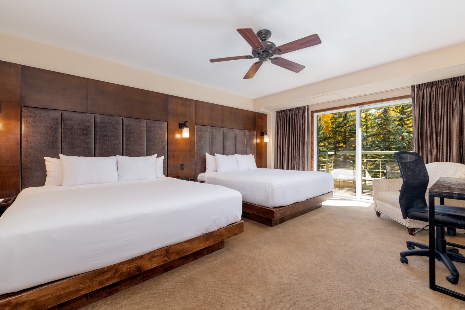 A Two King room at The Peaks: two white king beds against tall leather headboards, and a sliding door onto a balcony over the pines.