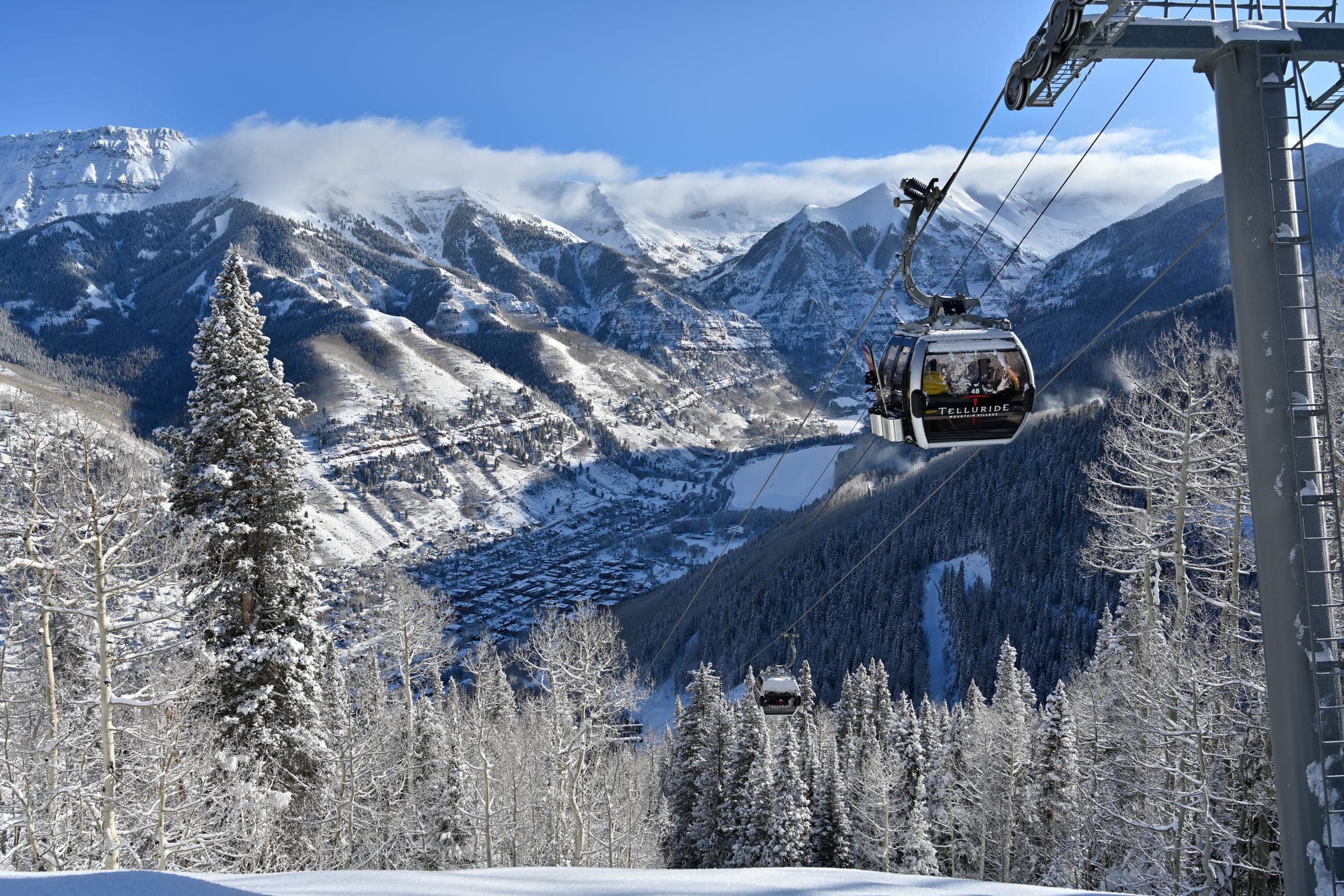 A gondola cabin crossing a snowy ridge, the town far below in the valley.