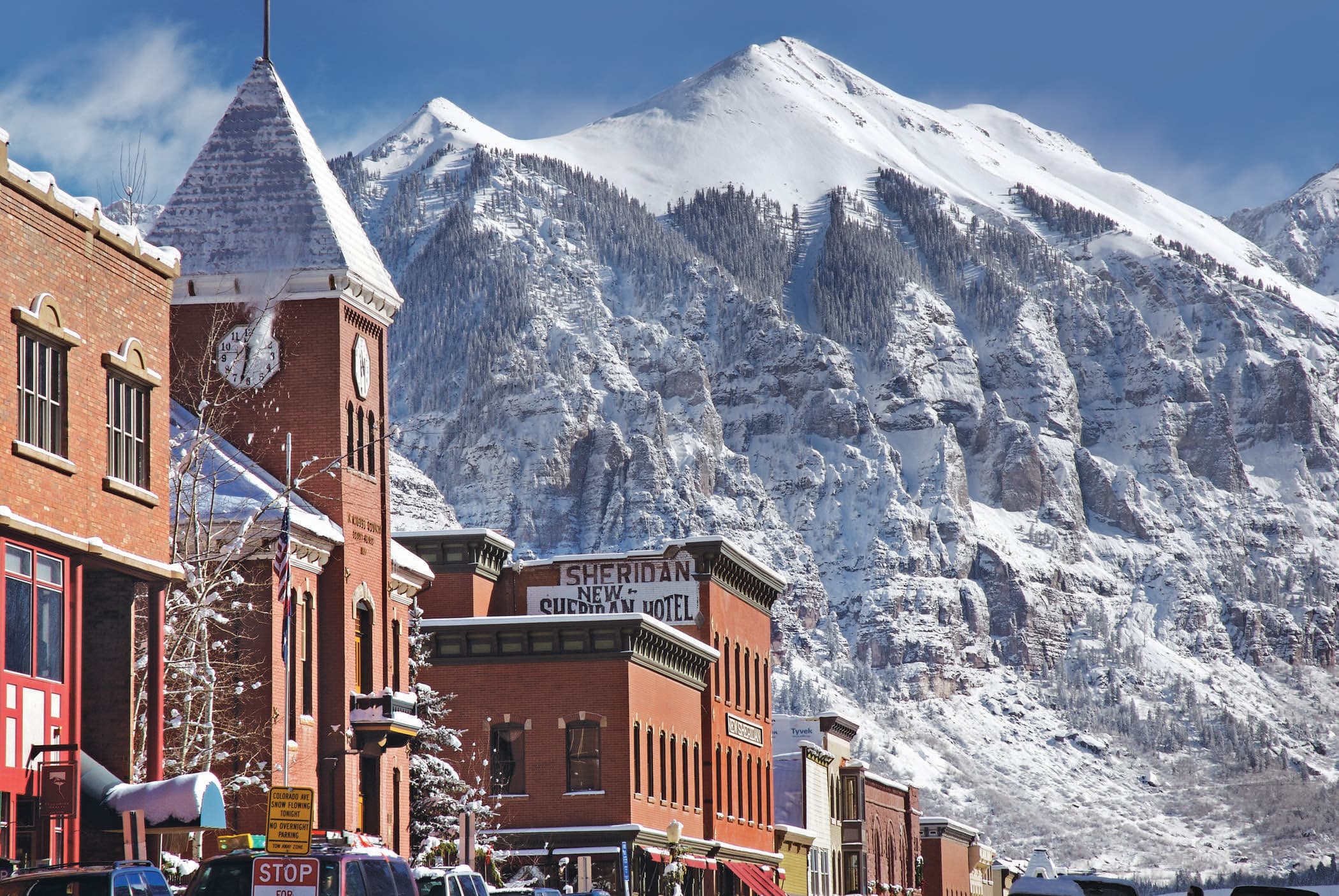 Telluride's brick Main Street and clock tower, a snow-covered peak rising straight up behind.