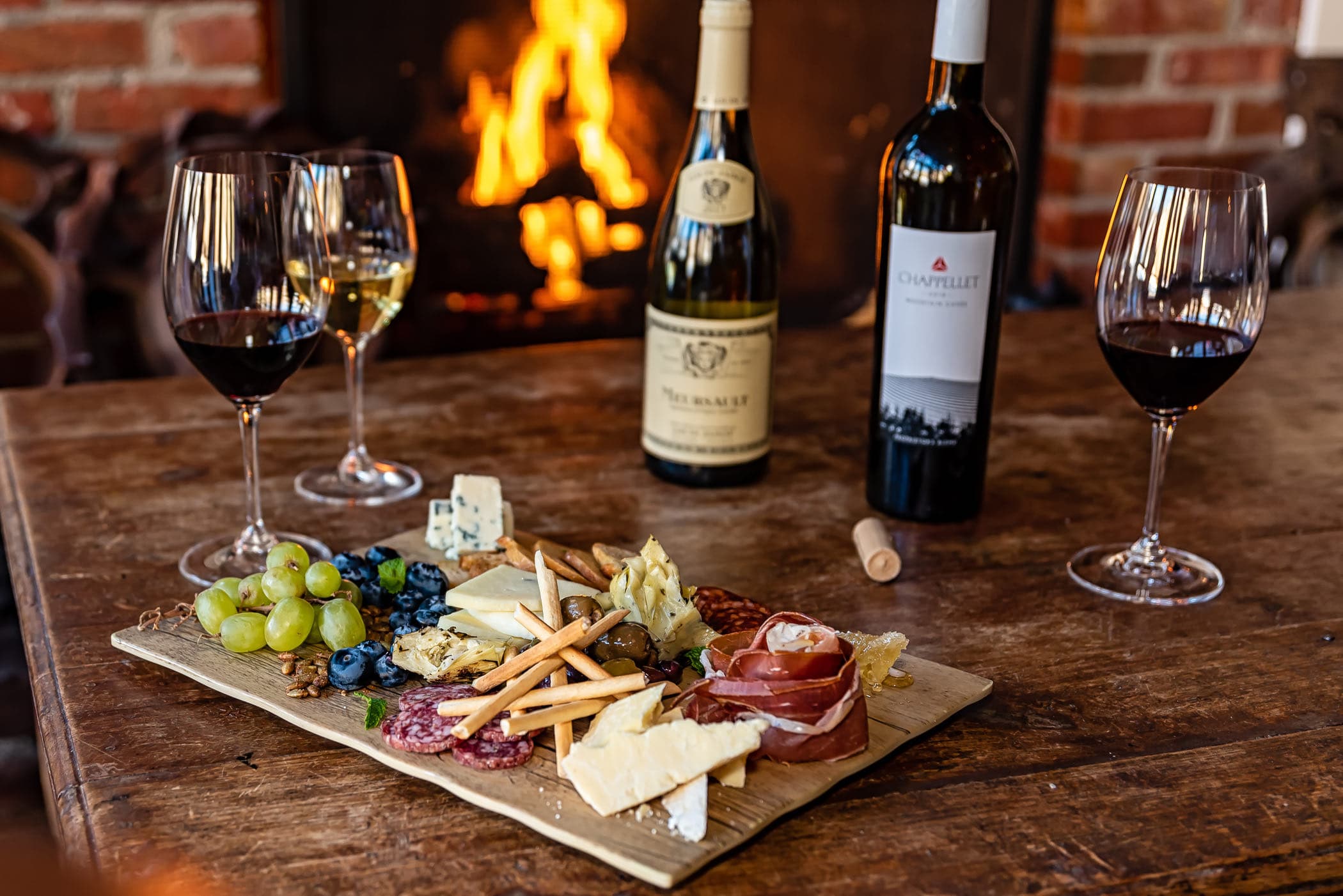 Wine and a board of food set out by a fire.
